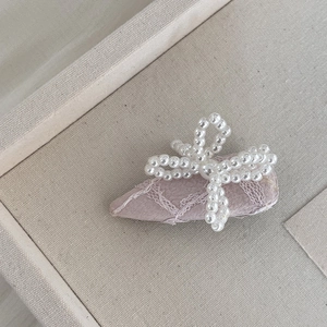 Détail d'une barrette en tissu rose avec dentelle blanche et nœud en perles blanches
