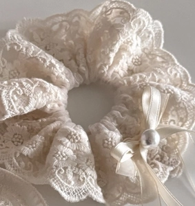 Dettaglio di un elastico in pizzo color crema con fiocco in raso e decoro di perla