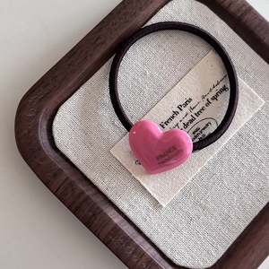 Détail d'un charme coeur en résine rose avec lettrage doré sur un élastique à cheveux noir