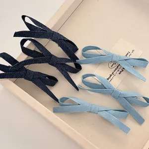 Detailed view of five denim bow hair clips in light and dark blue on a cream tray