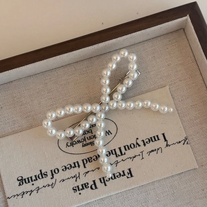 Elegant pearl bow hair clip with silver metal base on decorative fabric background