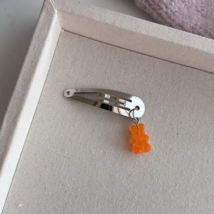 Zilveren metalen haarclip met oranje hars gummybeer hanger op een zachte achtergrond