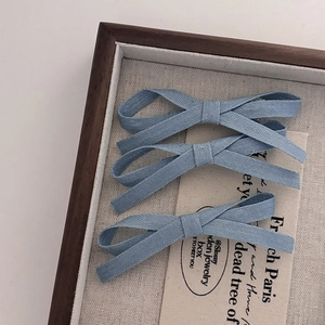 Three-piece blue denim bow hair clip set with fine canvas texture on a tray