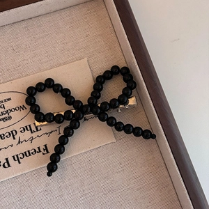 Detail of beaded black bow hair clip on a silver metal duckbill base in a wooden tray