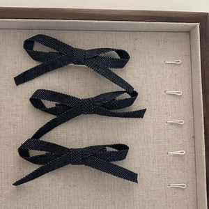 Three-piece set of navy denim fabric bow hair clips displayed on a beige jewelry tray