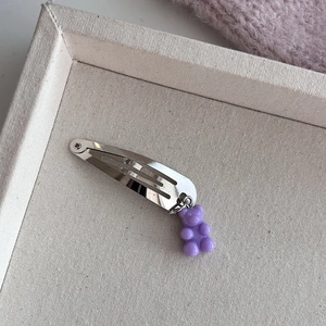Detailopname van een zilveren haarclip met een paars gummibeertje hanger van hars