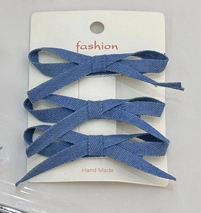 Detailed view of three blue denim fabric bow hair clips arranged on a white display card