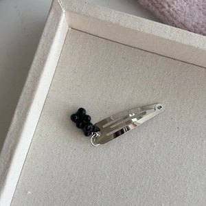 Gedetailleerd beeld van een zilveren haarspeld met een glanzende zwarte beerhanger van hars
