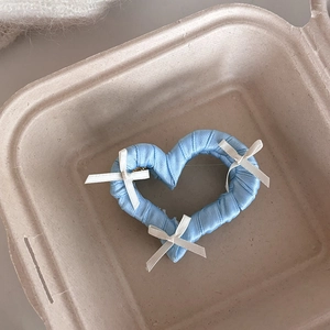 Dettaglio molletta per capelli a cuore azzurro con fiocchi bianchi in posa estetica