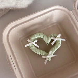 Dettaglio di un fermaglio a cuore in raso verde chiaro con piccoli fiocchi bianchi
