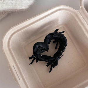Dettaglio di un mollettone a cuore nero con fiocchi di nastro sottili in una scatola