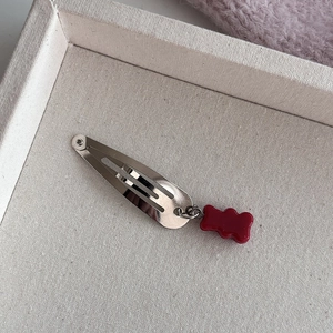 Zilveren metalen haarclip met een rode gummibeer hanger op een neutrale canvas achtergrond