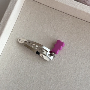 Detail van een zilveren snap-haarklem met een paarse harsbeer hanger op getextureerde basis