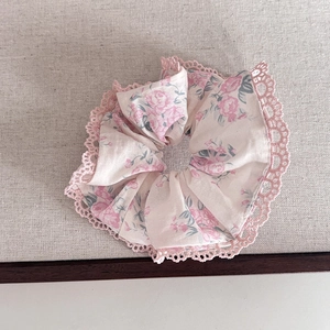 Vue détaillée d'un chouchou floral avec bordure en dentelle rose sur fond crème