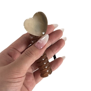 Brown heart-shaped hair claw clip with spiral bubble design held by hand on white background