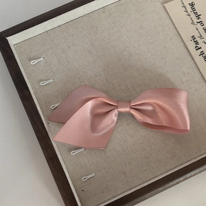 Elegant pink satin bow hair clip on a vintage linen tray for a French aesthetic look