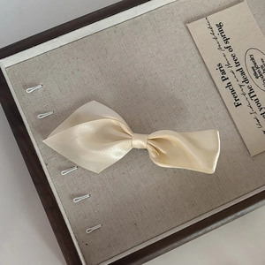 Elegant cream satin bow hair clip for women with French style aesthetic on wood tray