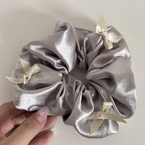 Detail view of silver satin scrunchie featuring elegant off-white ribbon bows