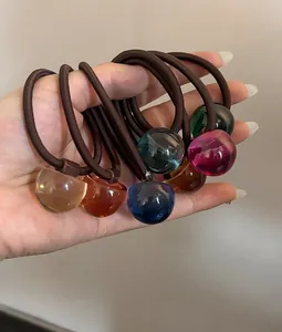 Dettaglio di perline in resina colorata traslucida su elastici per capelli in mano