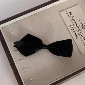 Detail view of black satin bow hair clip on a vintage linen and wooden jewelry tray