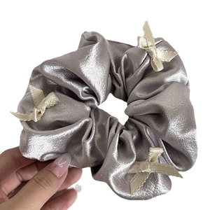 Chic silver metallic hair scrunchie featuring cream satin bows held by hand