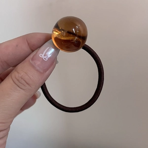 Dettaglio di un elastico per capelli marrone con perla in resina ambra traslucida