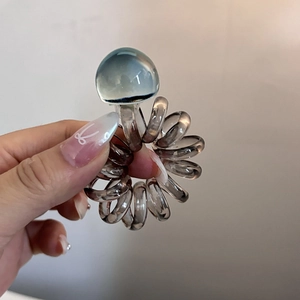 Close-up of translucent spiral hair coil with decorative bead on model's hand
