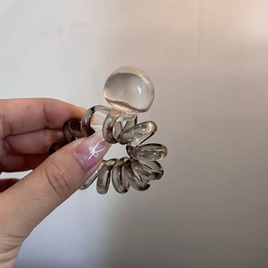 Detail of translucent grey spiral hair tie with clear bead held against neutral wall