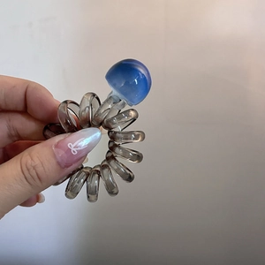 Macro detail of dark grey spiral phone cord hair tie with a blue-purple mushroom charm