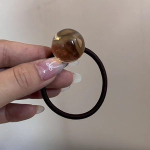 Dettaglio della sfera ambrata traslucida sull'elastico per capelli marrone elastico