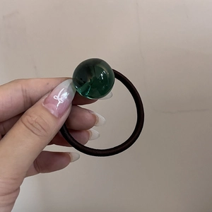 Dettaglio di un elastico per capelli con una perla verde traslucida per coda di cavallo