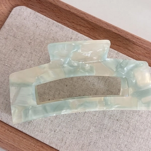 Close-up of hollow rectangular acetate hair claw with blue marble texture on wooden tray