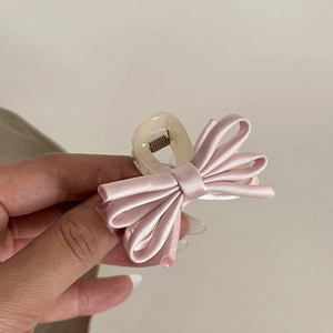 Close-up of a pink satin bow hair claw clip made of creamy resin with a metal spring