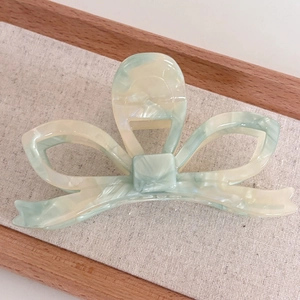 Close-up of bow-shaped acetate hair claw clip with light green marble texture