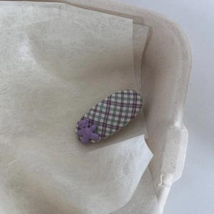 Close-up of cute bear hair clip with purple and green plaid fabric on yellow paper