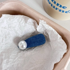 Barrette en denim à pois avec grande perle blanche sur un fond décoratif minimaliste