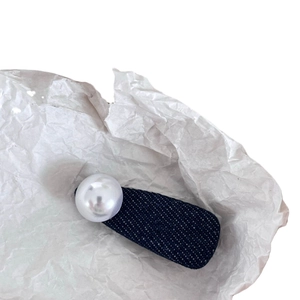 Barrette en tissu denim avec une grande perle blanche sur un fond blanc minimaliste