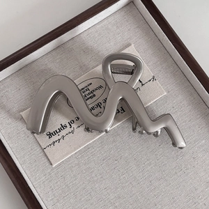 Macro detail of wave-shaped silver metal hair claw clip with focus on high-quality alloy texture