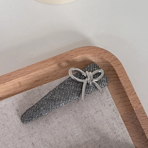 Sparkly silver bow hair clip on a minimalist wooden tray with soft linen fabric background