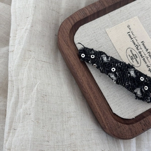 Close-up of black tweed hair clip with silver sequins on a wooden display tray