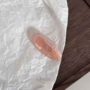 Detailed macro view of an oval pink acetate hair clip with golden handmade logo print