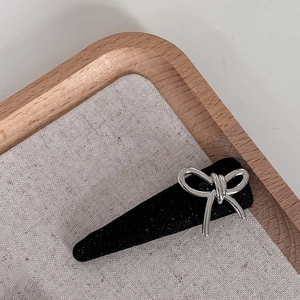 Close-up of a black glitter hair clip featuring a sleek silver metal bow decoration