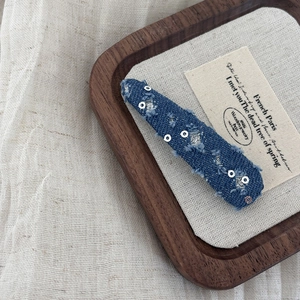 Close-up of distressed denim hair clip with silver sequins and fraying edge details