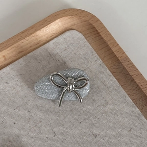 Detail view of silver bow hair clip with gray glitter teardrop base on wooden tray