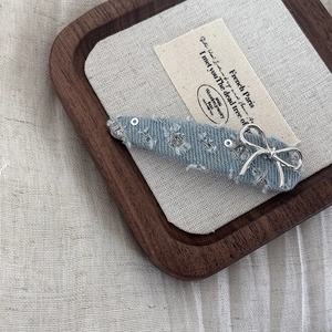 Close-up of light blue denim bow hair clip with silver hardware and sparkling rhinestones