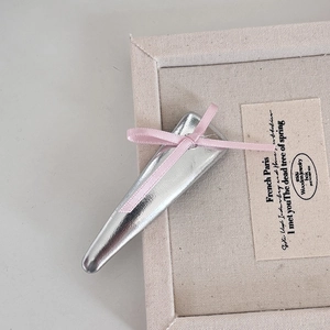 Détail de la pince à cheveux argentée avec nœud rose délicat sur plateau en bois