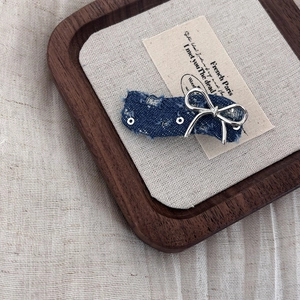 Detailed macro view of denim fabric hair clip with silver bow accent and distressed edges