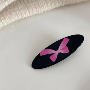 Elegante molletta ovale nera con fiocco rosa su sfondo bianco testurizzato e pulito