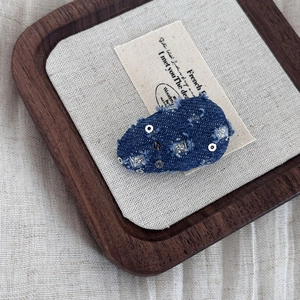 Blue denim hair clip with silver sequins and frayed edges on a wooden display tray