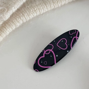 Dettaglio molletta ovale nera con cuori rosa e stelle su sfondo di maglia bianca
